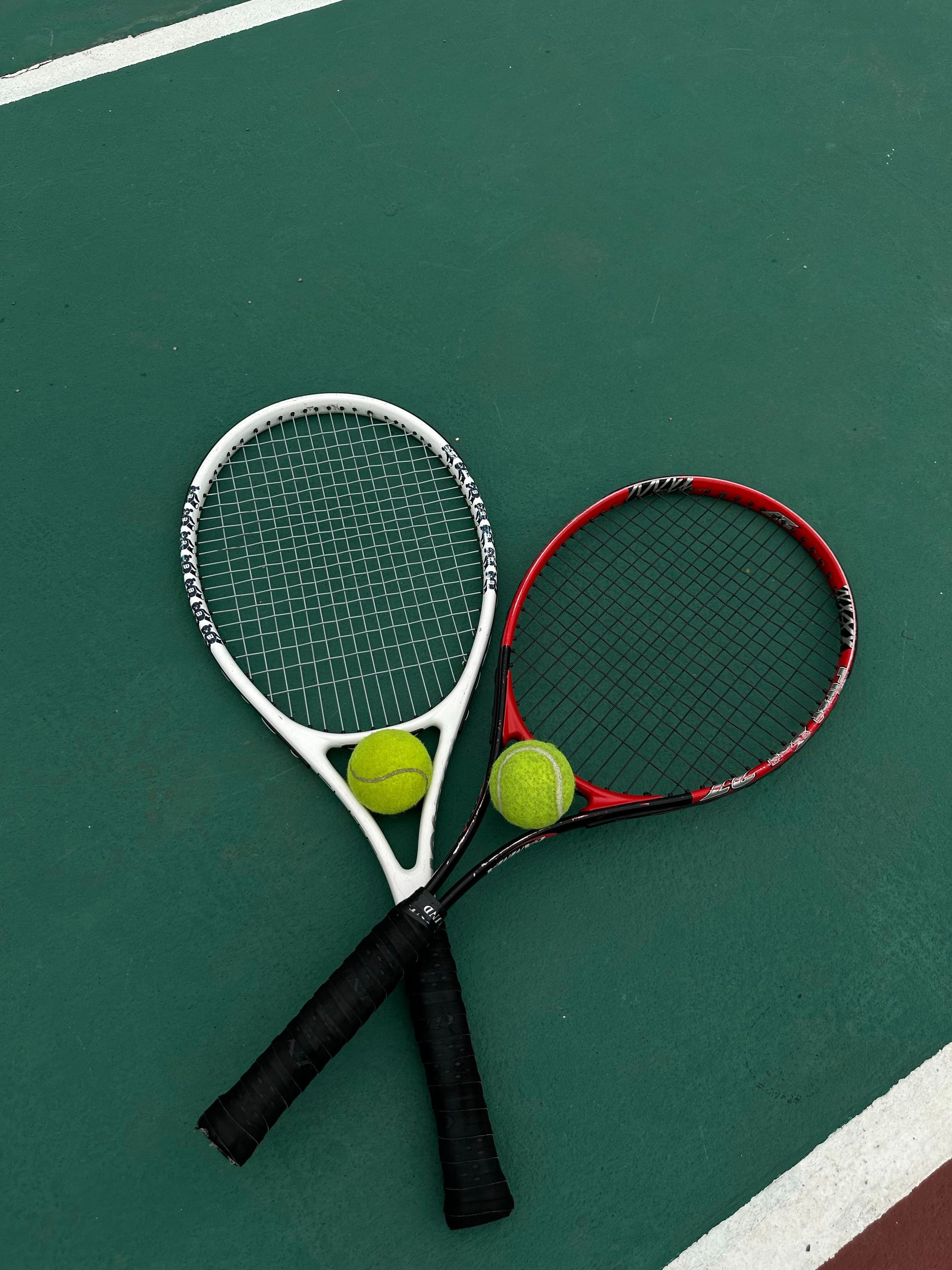 Two tennis rackets and balls on a green court, ready for a match.